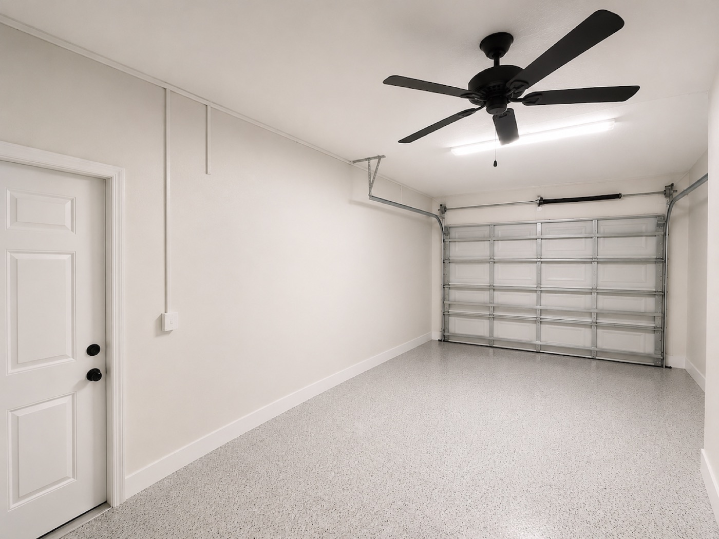 Clean empty garage with white walls, ceiling fan, and speckled epoxy floor after renovation